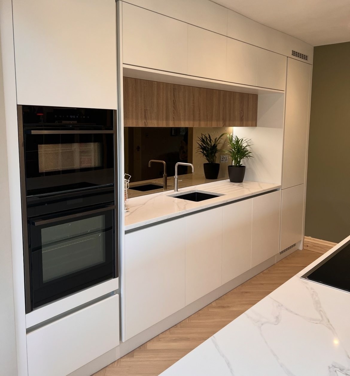 Handleless white kitchen with oak accents and a marble-effect splashback, installed by Studio Seven